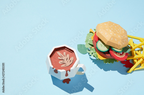 A cup of coffee with cheeseburger and french fries is made from paper craft on a blue background photo