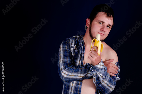 Cute man in a blue shirt, naked body, blue background and banana.