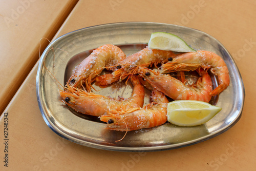 Cooked shrimp accompanied by lemon in a stainless steel bowl on a table