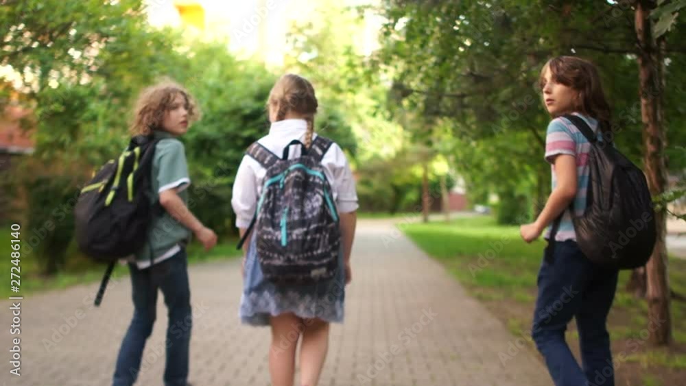 Cheerful teens are returning from school, laughing and hustling, carrying their backpacks, rear view. Back to school Cheerful teens are returning from school, laughing and hustling, carrying their backpacks, rear view. Back to school