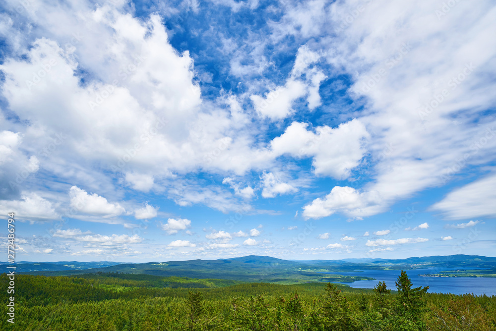 Blue sky with white clouds over the mountaneous landscape of Šumava nature preserve. View from lookout tower in castle ruins of Vítkův hrádek. The Lipno Reservoir in the background. Czech republic.