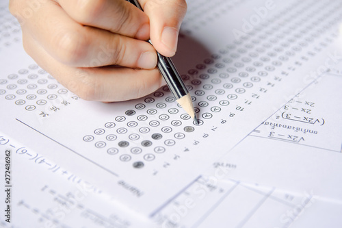 Students hand holding pencil writing selected choice on answer sheets and Mathematics question sheets. students testing doing examination. school exam