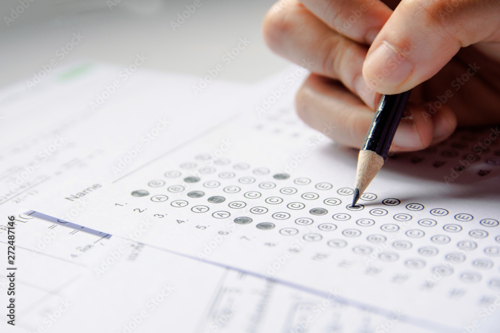 Students hand holding pencil writing selected choice on answer sheets and Mathematics question sheets. students testing doing examination. school exam Students hand holding pencil writing selected choice on answer sheets and Mathematics question sheets. students testing doing examination. school exam