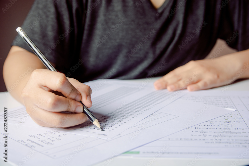 Students hand holding pencil writing selected choice on answer sheets and Mathematics question sheets. students testing doing examination. school exam Students hand holding pencil writing selected choice on answer sheets and Mathematics question sheets. students testing doing examination. school exam