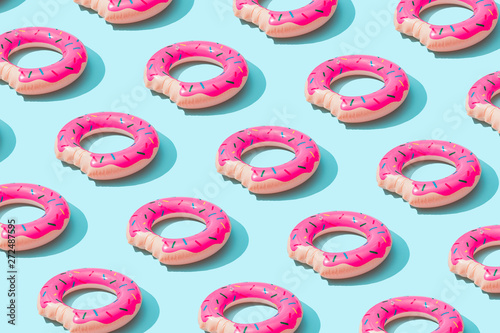 Trendy sunlight Summer pattern made with pink doughnut inflatable toy on bright light blue background. Minimal summer concept.