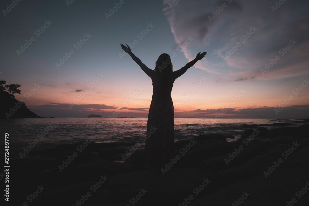 Happy young woman in dress enjoys her tropical beach vacation in sunset