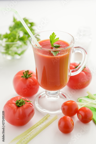 Tomato juice is poured into a transparent glass with parsley and herring, on a white background with cherry tomatoes, lit by sunlight