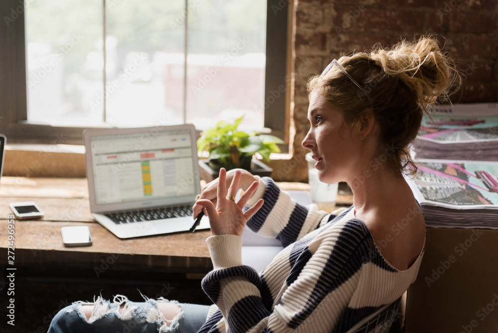 © jamie grill photography/Stocksy - Woman talking to co-worker while using laptop