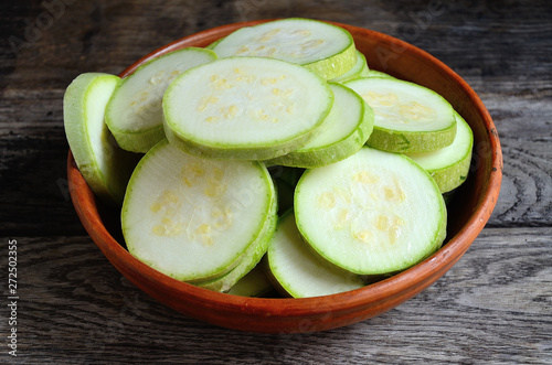 Sliced zucchini in a ceramic bowl on a rustic wooden table.
