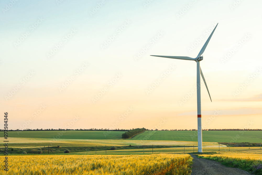Wind turbine and beautiful fields at sunset, space for text