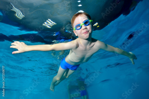 Smiling sports boy swimming underwater, at the surface of the water. Arms outstretched like a bird. Posing for the camera with his eyes open. Portrait. Photo underwater. Horizontal view