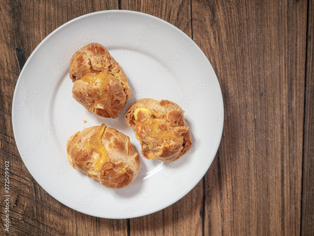 Three cream puffs on a white plate filled with custard and topped with sweet syrup. Close up.