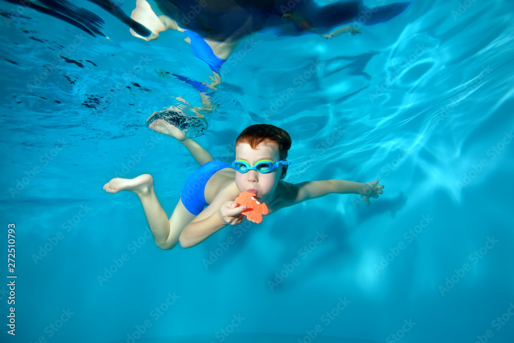 Little sports boy swimming underwater in the pool, posing with a toy in his hands and looking at the camera . Portrait. Underwater photography. Horizontal orientation