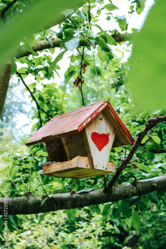 Lovely birdhouse with a red roof and a heart on the front hanging in a garden.