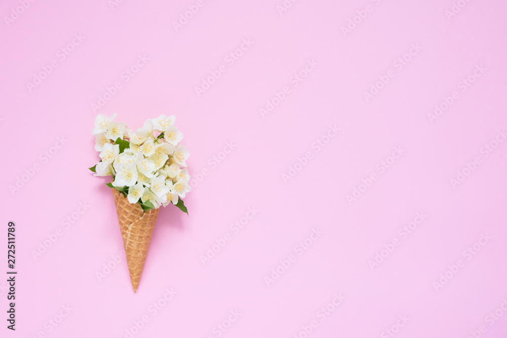 Fototapeta Philadelphus or mock-orange flowers in a waffle ice cream cone on pink background. Summer concept. Copy space, top view.