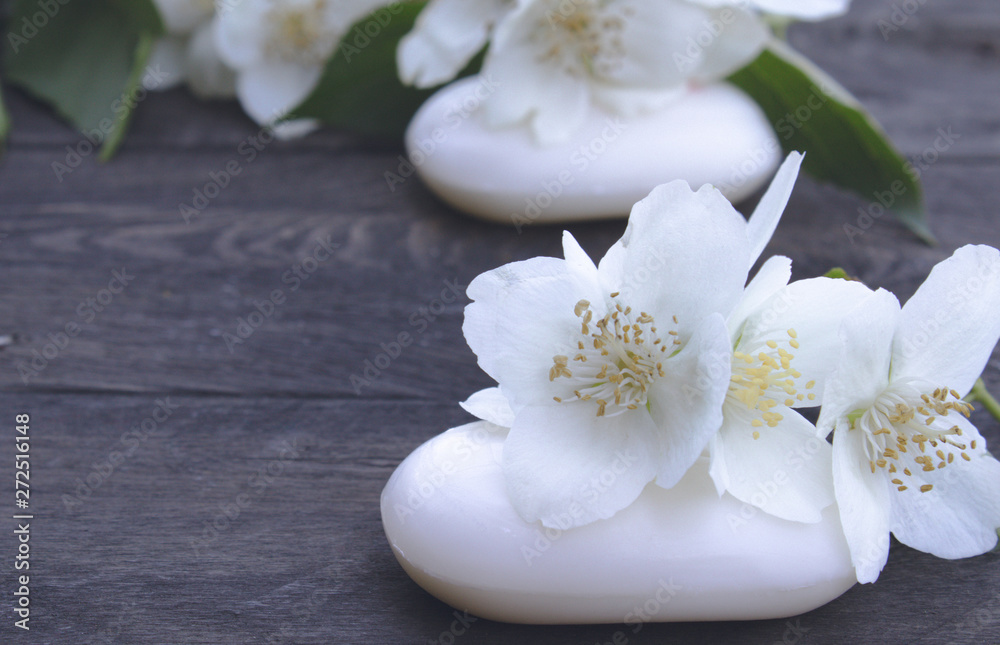 Cosmetic soap and white jasmine flowers with green leaves lie on a wooden background. There is a place for your text. Cosmetic soap and white jasmine flowers with green leaves lie on a wooden background. There is a place for your text.
