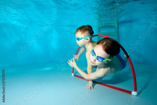 Two beautiful boys play sports under water in the pool. Swim through the Hoop in the water. Bottom view from the bottom of the pool. Portrait. Underwater photography. Horizontal view