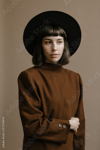 woman in hat wearing vintage style brown jacket against light brown backdrop
