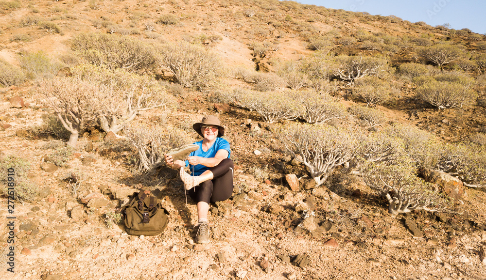Smiling old woman removes the pebbles from her shoes. Trekking with backpack on the arid volcanic mountain. One happy caucasian people Smiling old woman removes the pebbles from her shoes. Trekking with backpack on the arid volcanic mountain. One happy caucasian people