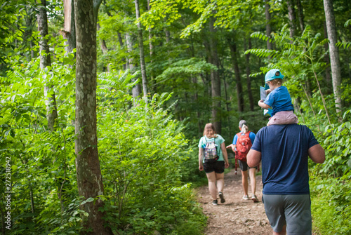A family of hikers, three adults and one child on a man's shoulders reading a map hiking though the forest in Shenandoah National Park . 