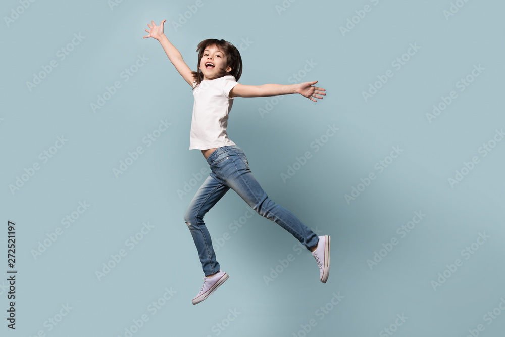 Full length funny little girl jumping isolated on blue background