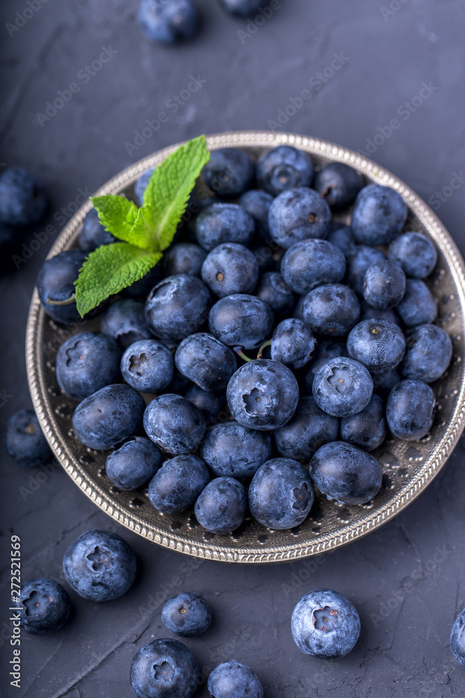 ripe, large blueberries in a metal plate, with a leaf of mint, on a dark gray stone table, top view ripe, large blueberries in a metal plate, with a leaf of mint, on a dark gray stone table, top view