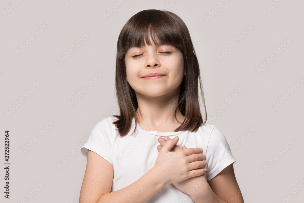Little girl closed eyes hold hand on chest feels gratitude - obrazy, fototapety, plakaty 