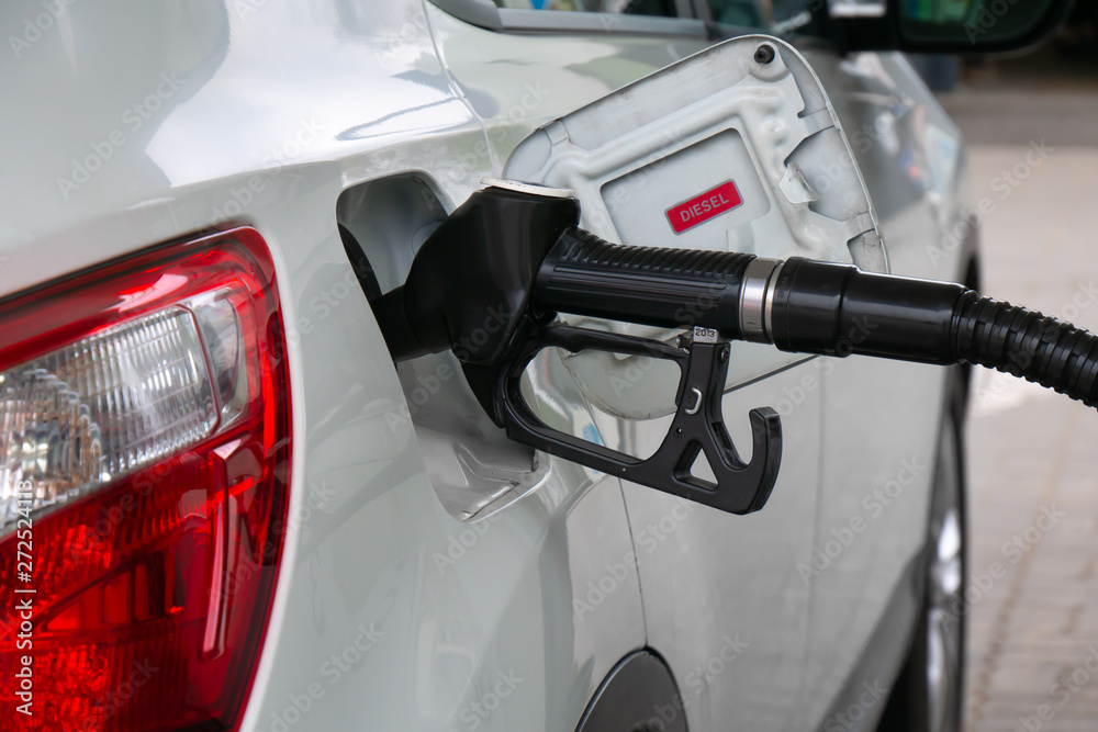 Refueling the car. Black fuel dispenser inserted in white diesel automobile with red rear light. Refueling the car. Black fuel dispenser inserted in white diesel automobile with red rear light.