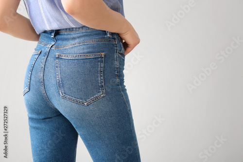Young woman wearing stylish jeans pants on light background © Pixel-Shot