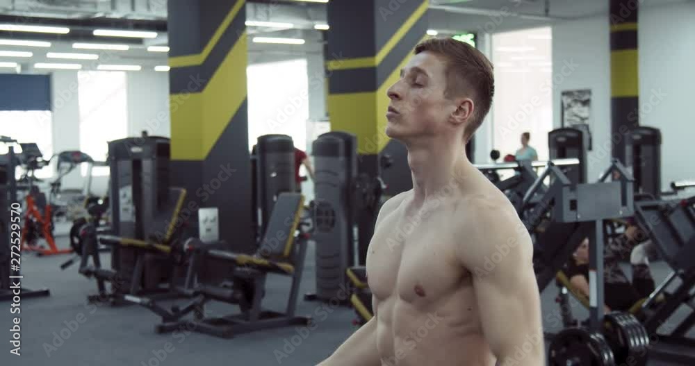 A bare-chested athlete stretches his arms in the gym