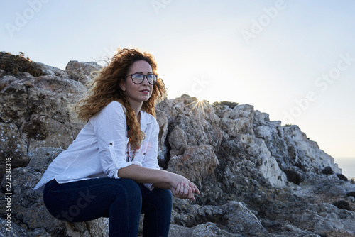 Thoughtful woman sittin on stones at cliff at sunset. photo