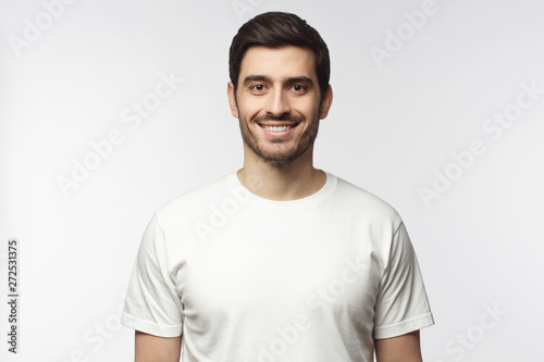 Portrait of smiling young man in white t-shirt looking at camera, isolated on gray background
