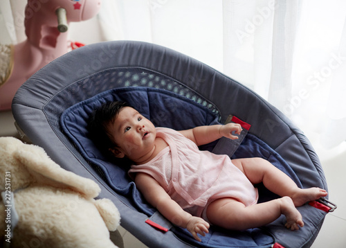 Cute Asian baby, sitting on a small lounger and playing with himself,  at home