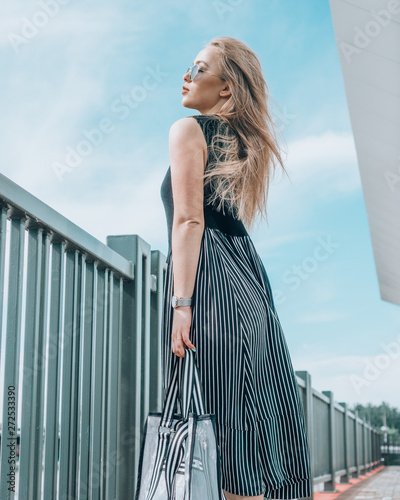 Beautiful girl in glasses and a handbag posing on the waterfront near the fence