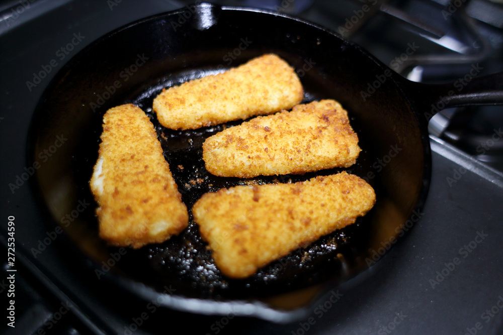 Breaded fish sticks baked in a cast iron skillet, resting on the stove. Breaded fish sticks baked in a cast iron skillet, resting on the stove.