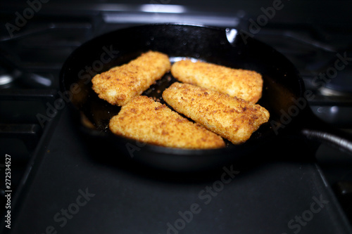 Breaded fish sticks baked in a cast iron skillet, resting on the stove.