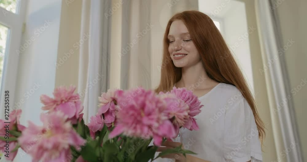 Attractive girl put the flowers of peonies in a vase and corrects the bouquet. Red-haired woman enjoying the fresh flowers and aroma of peonies. tracking shot. in slow motion. Shot on Canon 1DX mark2 Attractive girl put the flowers of peonies in a vase and corrects the bouquet. Red-haired woman enjoying the fresh flowers and aroma of peonies. tracking shot. in slow motion. Shot on Canon 1DX mark2