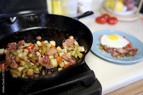 Corned beef hash frying in a cast iron skillet on a natural gas stove top in a home kitchen.