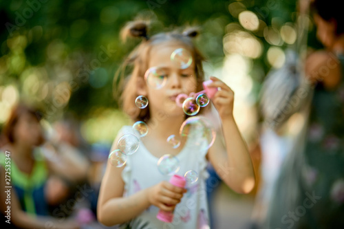 blurred cute baby girl is making soap bubbles in the park on summer day