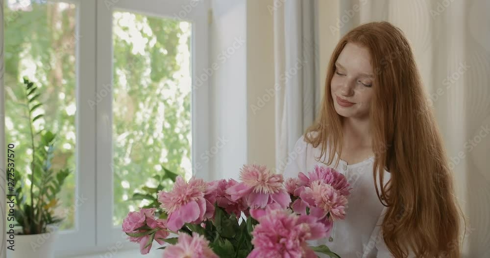 Attractive girl put the flowers of peonies in a vase and corrects the bouquet. Red-haired woman enjoying the fresh flowers and aroma of peonies. tracking shot. in slow motion. Shot on Canon 1DX mark2 Attractive girl put the flowers of peonies in a vase and corrects the bouquet. Red-haired woman enjoying the fresh flowers and aroma of peonies. tracking shot. in slow motion. Shot on Canon 1DX mark2