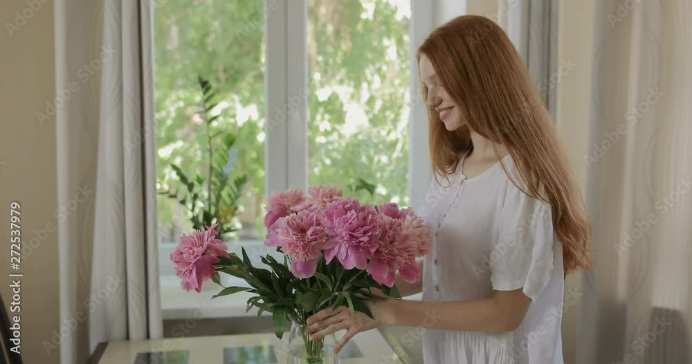 Attractive girl put the flowers of peonies in a vase and corrects the bouquet. Red-haired woman enjoying the fresh flowers and aroma of peonies. tracking shot. in slow motion. Shot on Canon 1DX mark2 Attractive girl put the flowers of peonies in a vase and corrects the bouquet. Red-haired woman enjoying the fresh flowers and aroma of peonies. tracking shot. in slow motion. Shot on Canon 1DX mark2