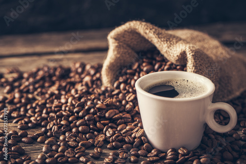 Canvas Print Coffee cup with coffee beans on wood background.