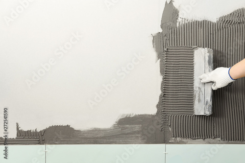 Closeup of worker spreading concrete on wall with spatula, space for text. Tile installation