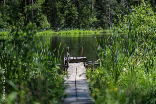 nice wooden plank boardwalk leans into blue lake with green shores and blue sky