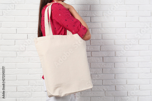 Woman with stylish blank eco bag near brick wall, closeup. Space for text