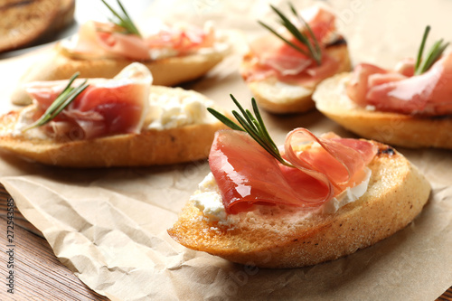 Tasty bruschettas with prosciutto and cream cheese on parchment, closeup