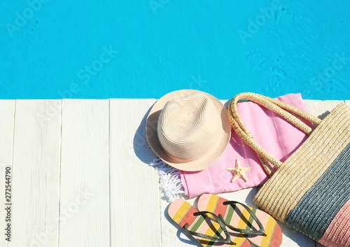 Beach accessories on wooden deck near swimming pool, top view. Space for text