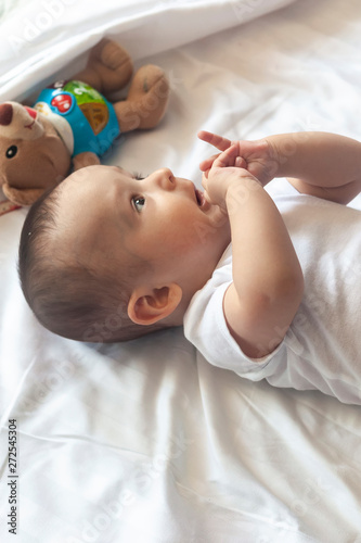 6-8-month-old baby boy lying playfully in bed. Charming 6-7 month little baby in white bodysuit. Baby boy in white bedding. Copy space