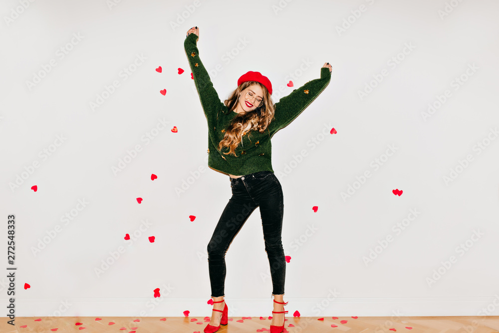 Blissful girl in red high heel shoes dancing on white background under heart confetti. Spectacular young woman in french beret having fun in valentine's day. - obrazy, fototapety, plakaty 