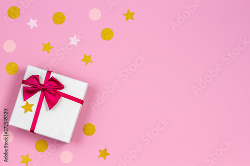 Festive gift box with satin bow and glitter confetti sparkles on light pastel pink background. Top view © vejaa